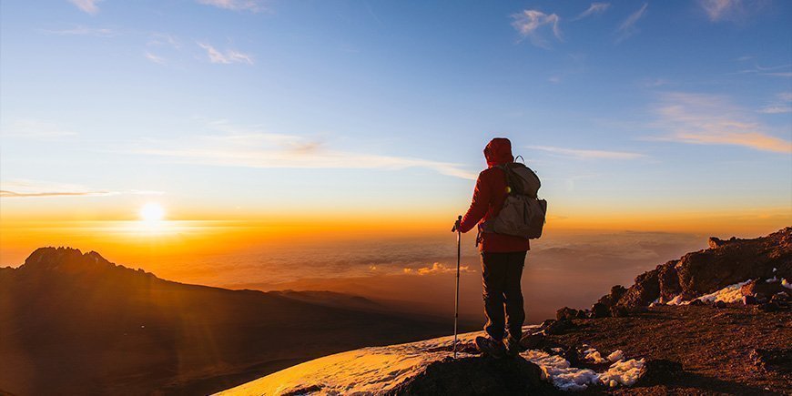 Mand står på Kilimanjaro i solopgangen